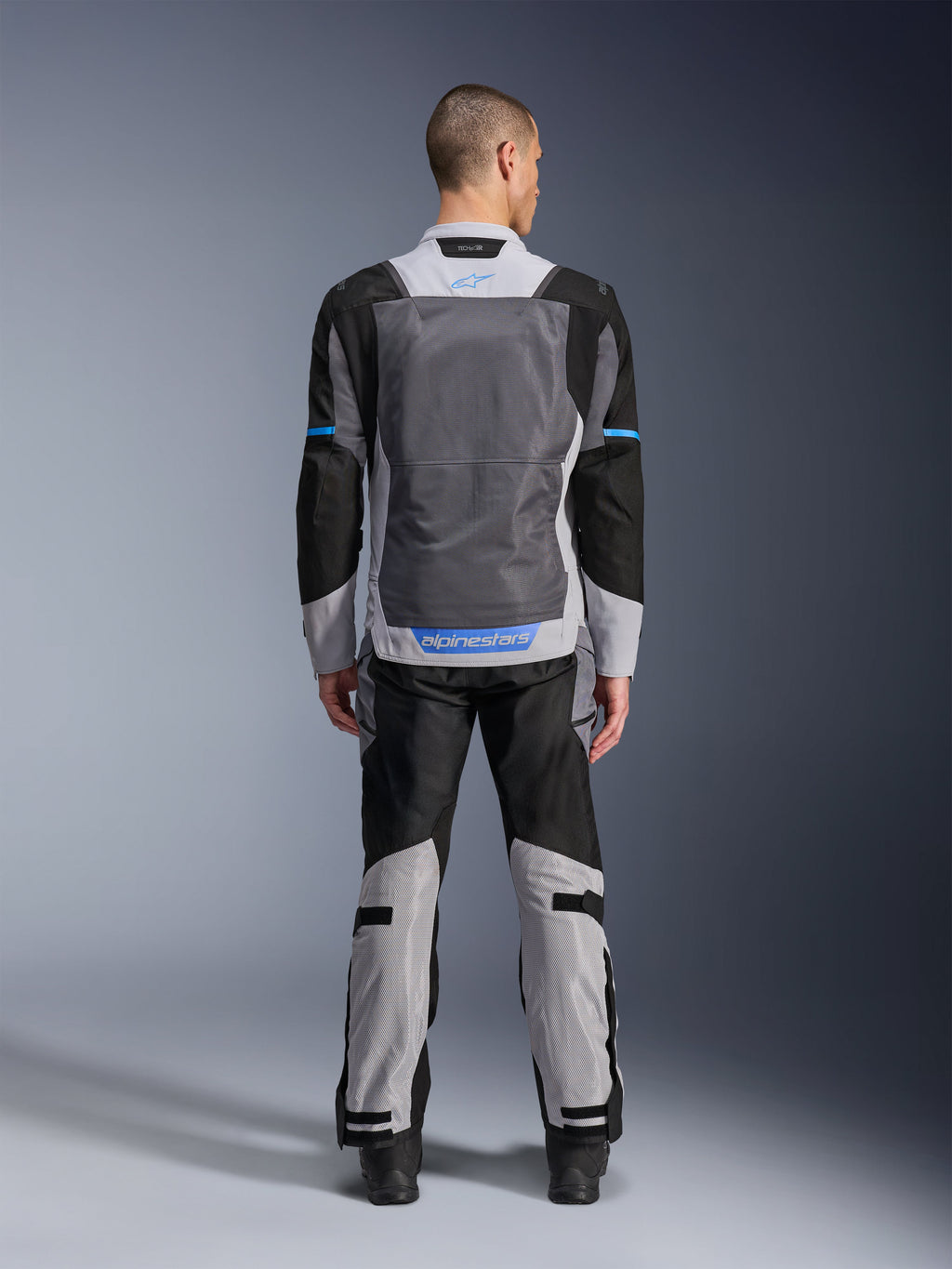 Alpinestars ST-2 Air Jacket, Ice Gray Dark Gray Black, rear view on model, featuring large mesh ventilation panels, blue accents and Alpinestars logo, paired with matching motorcycle pants for adventure touring.