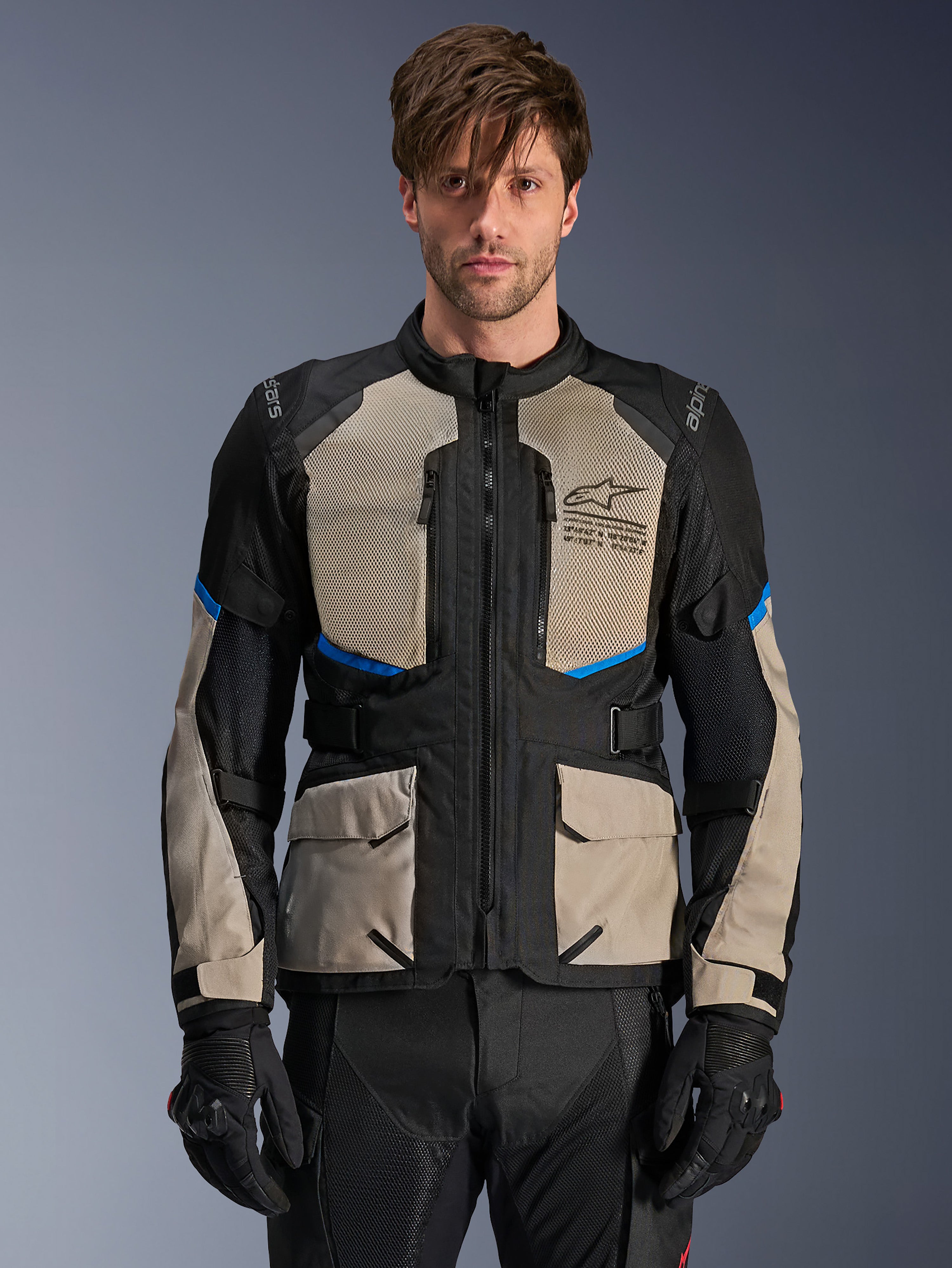 Alpinestars Andes Air Drystar Jacket, Adventure Touring Jacket, Black Laurel Gray and Bright Blue, worn by a model with black gloves, featuring large mesh chest panels for airflow, front cargo pockets, and blue accents, protective motorcycle touring gear