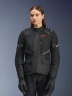 Alpinestars Stella Andes Air Drystar Jacket, Women's Motorcycle Touring Jacket, Black with gray accents and a small red logo, featuring mesh ventilation panels, a high collar, and multiple utility pockets, worn with matching riding gloves and pants