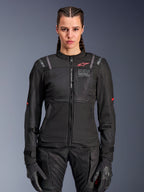 Alpinestars Woman Stella ST-2 Air Jacket, Women's Motorcycle Jacket, Black, front view on model, featuring mesh panels, red logo on chest, and Alpinestars Exploration Equipment branding, worn with black gloves and riding pants