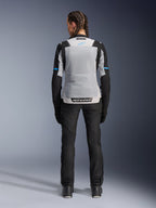 Alpinestars Stella ST-2 Air Jacket, Ice Gray Black, rear view on female model, featuring a large light gray mesh back panel, black sleeves with blue stripe accents, Alpinestars branding on the lower back, paired with black technical riding pants and boots, summer motorcycle touring gear