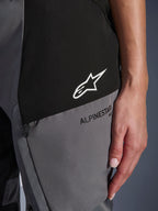 Close-up of Alpinestars Woman Stella Andes V4 Drystar® Pants in Black and Dark Gray, featuring a white star logo on a black panel and black Alpinestars branding on a gray panel, showing technical textile fabric and zippered pocket detail.