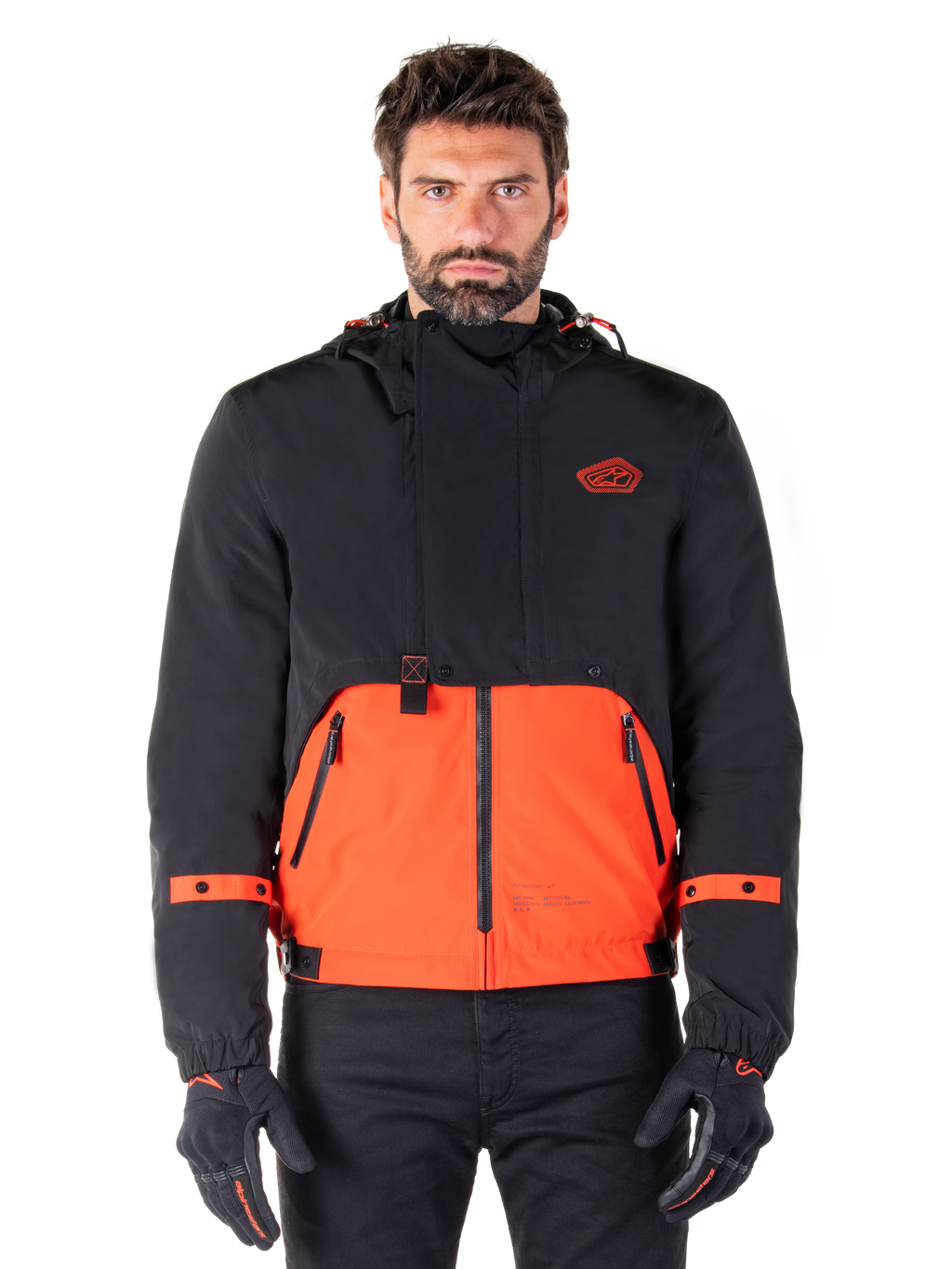 Alpinestars Mootant Waterproof Parka, modular motorcycle jacket in Spicy Orange and Black, worn by a model with matching gloves, features a hooded design with two-tone panels, front zipper, and adjustable cuffs, urban contemporary riding apparel