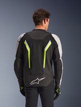 Alpinestars AST V3 Air Jacket, Black Silver Yellow Fluo, rear view on model, textile motorcycle jacket featuring dual tech mesh ventilation panels, vertical neon yellow stripes, silver sleeves, and a white Alpinestars logo on the lower back.