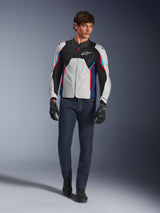 Male model wearing the Alpinestars AST V3 Air Jacket in Silver Deep Blue Bright Red, featuring mesh ventilation and perforated panels, paired with dark denim riding jeans and black gloves, sport-optimized motorcycle gear for warm weather.