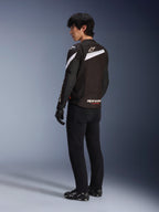 Male rider wearing the Alpinestars T-GP Plus R V4 Jacket in Black and White, rear view showing white diagonal accents and branding on the lower back, paired with black riding pants, gloves, and technical boots, sport-fit textile motorcycle gear