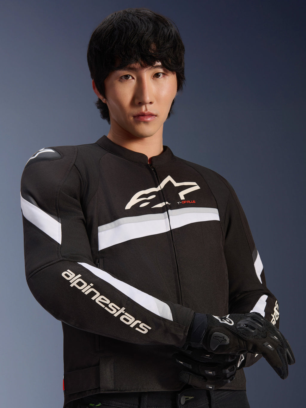 Alpinestars T-GP Plus R V4 Jacket, Black and White, worn by a male model, textile motorcycle jacket with white stripes across the chest and sleeves, Alpinestars logo on the chest, paired with black riding gloves