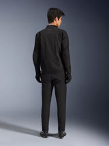Alpinestars Aeroshell Airflow Jacket in Black Anthracite, back view of a male model wearing full motorcycle riding gear including black pants and gloves, featuring a lightweight softshell construction with an elongated rear for coverage.