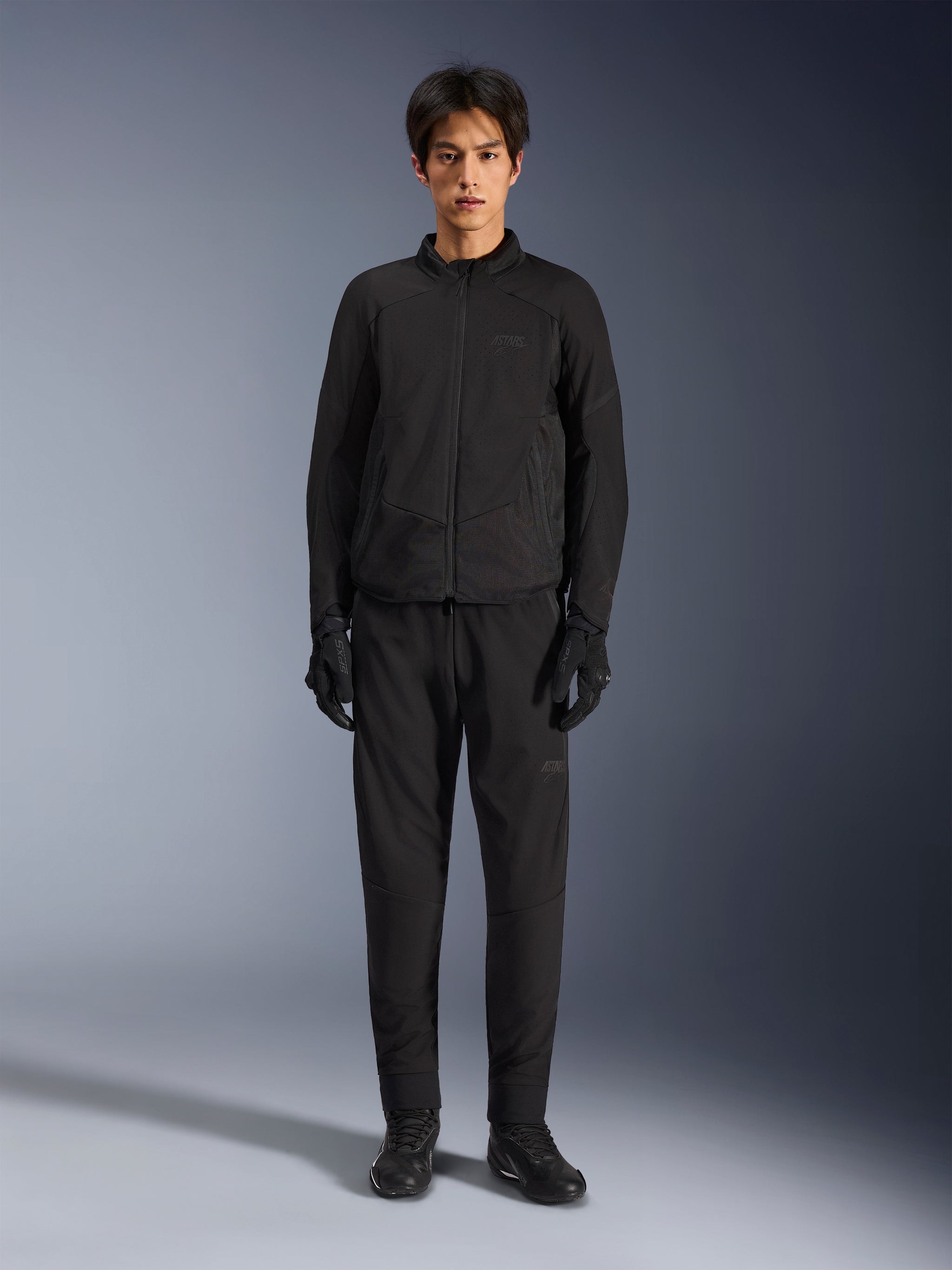 Alpinestars Aeroshell Airflow Jacket, Black motorcycle jacket, worn by model with matching black pants and gloves, featuring laser-perforated chest and side mesh panels, sport-cut fit for warm-weather performance
