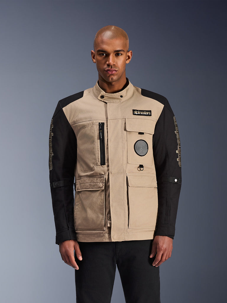 Alpinestars Dice Jacket, Urban Motorcycle Jacket, Beige and Black, rugged workwear aesthetic featuring multiple utility pockets and chest patches, high collar with button closure, bold branding on sleeves, worn by a male model