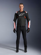Male model wearing Alpinestars T-Sps Air V2 Jacket in Black White Red Fluo, featuring large tech mesh panels and bold white branding on the chest and sleeves, paired with black technical riding pants and gloves, urban sport motorcycle gear