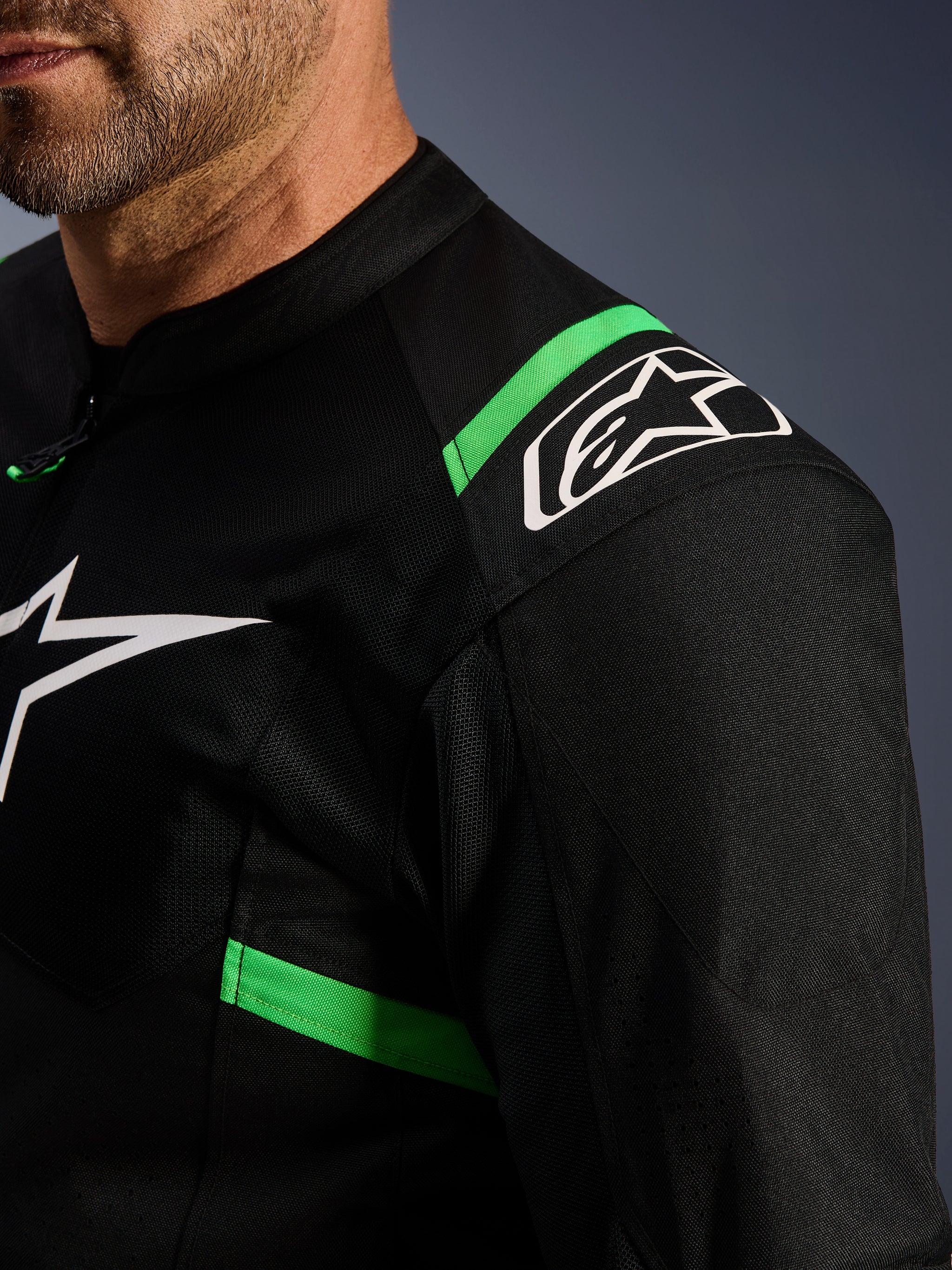 Alpinestars T-SPS Air V2 Jacket, Black and Fluo Green, close-up of shoulder and chest area, white Alpinestars star logo, technical mesh fabric for airflow, sporty motorcycle riding jacket