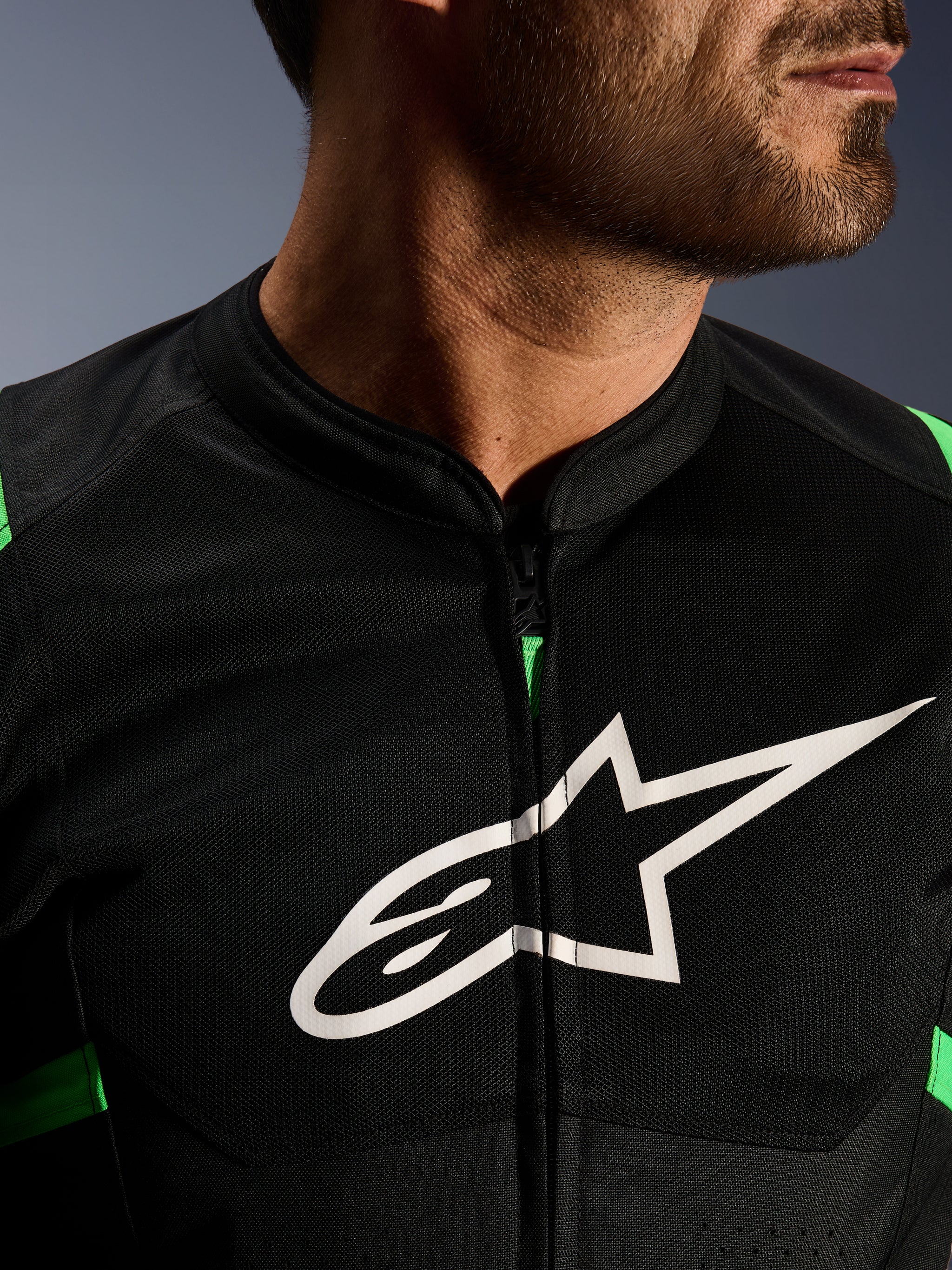 Close-up of Alpinestars T-SPS Air V2 Jacket, Black and Fluo Green, featuring breathable tech mesh panels, central zipper, and prominent white Alpinestars star logo on the chest, performance motorcycle gear