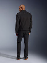 Alpinestars Bruiser Jacket in Black, back view of male model wearing the urban motorcycle jacket with matching black pants, featuring a small gold logo on the collar and adjustable waist straps, workwear-inspired aesthetic