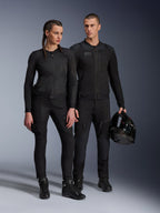 Alpinestars Stella Troop-Air Jacket, Man and woman wearing matching all-black technical motorcycle gear, featuring mesh construction for airflow, black pants and boots, man holding a black helmet, urban riding apparel.