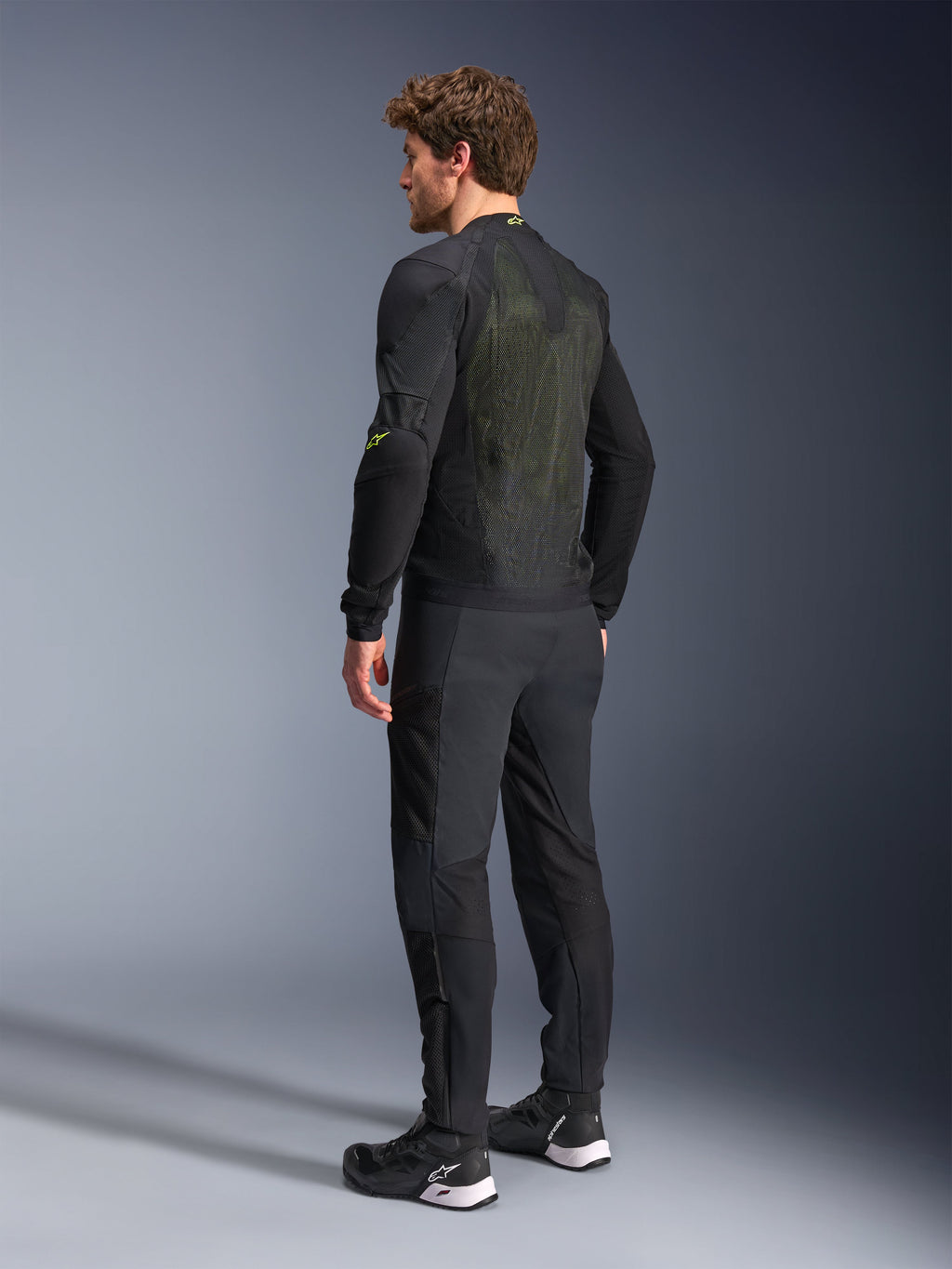 Alpinestars Troop-Air Jacket in Black and Yellow Fluo, rear view of a male model wearing the technical air jacket, featuring a large mesh back panel with yellow highlights and fluo yellow Alpinestars logos, paired with black motorcycle pants.