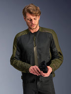 Man wearing the Alpinestars C-1 Air Jacket in Khaki, urban motorcycle jacket with olive green textile and black mesh panels, looking down while holding black motorcycle gloves, clean and contemporary style for road riding.