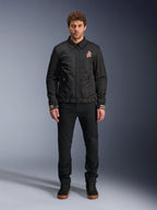 Male model wearing the Alpinestars Ignite Air Jacket in black, featuring a classic shirt collar, full front zipper, and an orange logo on the chest. Styled with black pants and black high-top sneakers for an urban contemporary motorcycle look.