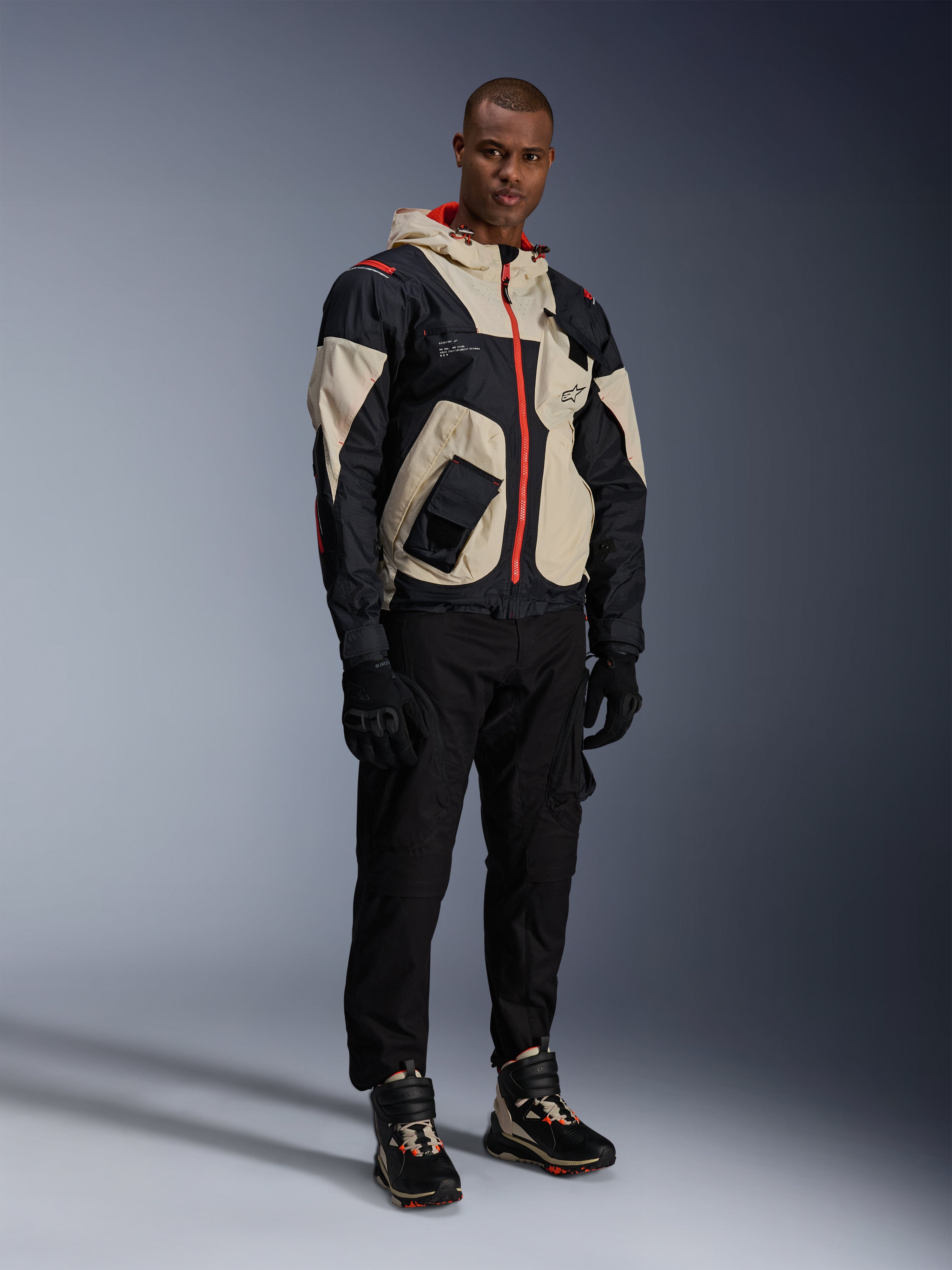 Alpinestars Acteon Pants, Black motorcycle pants, worn with a black, beige, and red Mogress Air Jacket, black riding gloves, and matching high-top riding sneakers, contemporary urban motorcycle gear for men