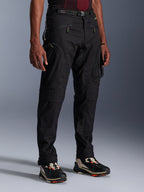 Alpinestars Acteon Pants, Black Motorcycle Pants, worn by a model, featuring a modern tapered silhouette, zippered cargo pockets, adjustable waist belt, and technical sneakers, urban riding apparel