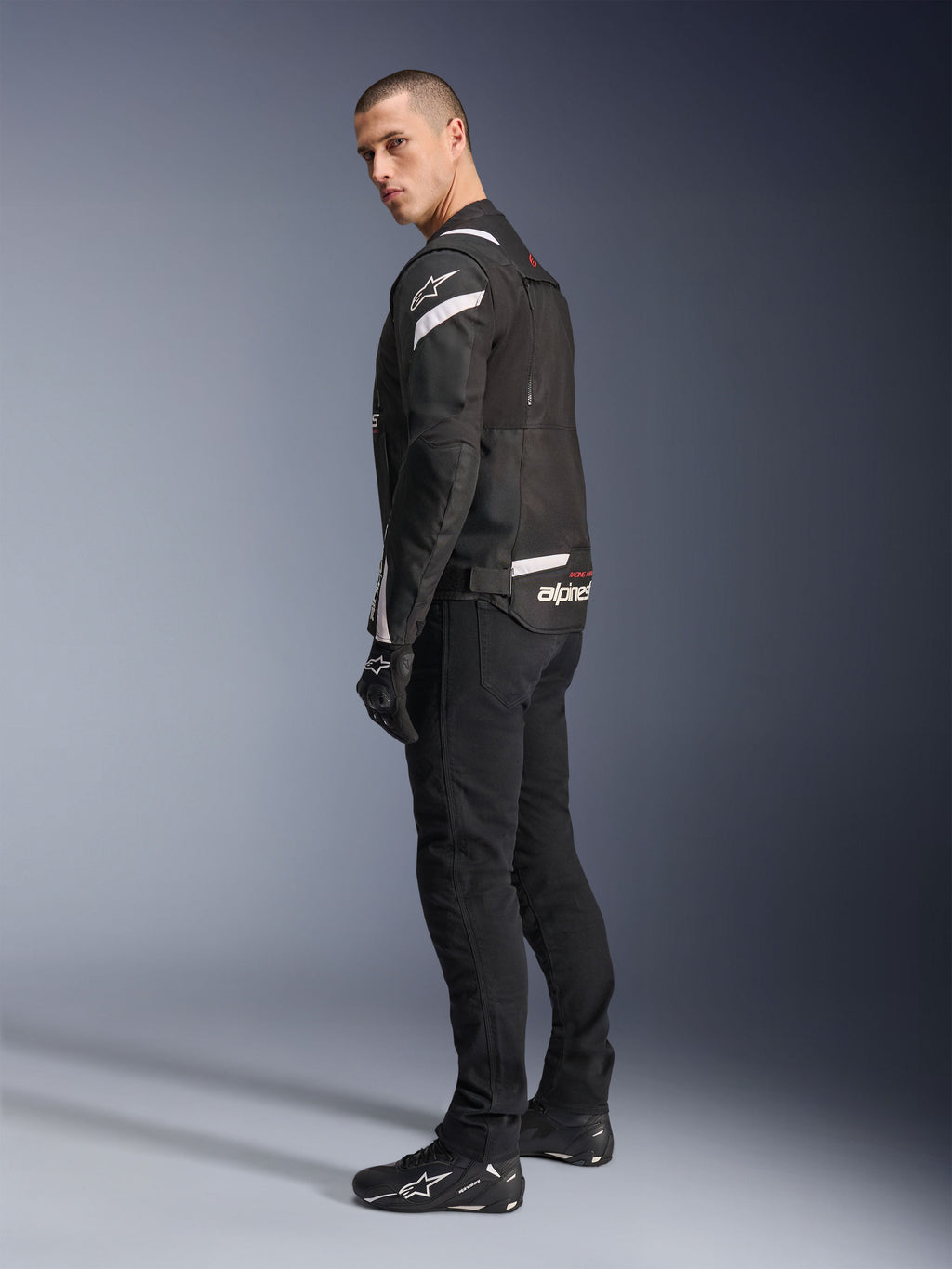 Alpinestars T-Stunt Air Jacket, Black and White, modular motorcycle jacket with tech mesh panels, shown from a back-side profile on a model, worn with black riding pants and shoes, featuring white accents and branding on the shoulders and back.