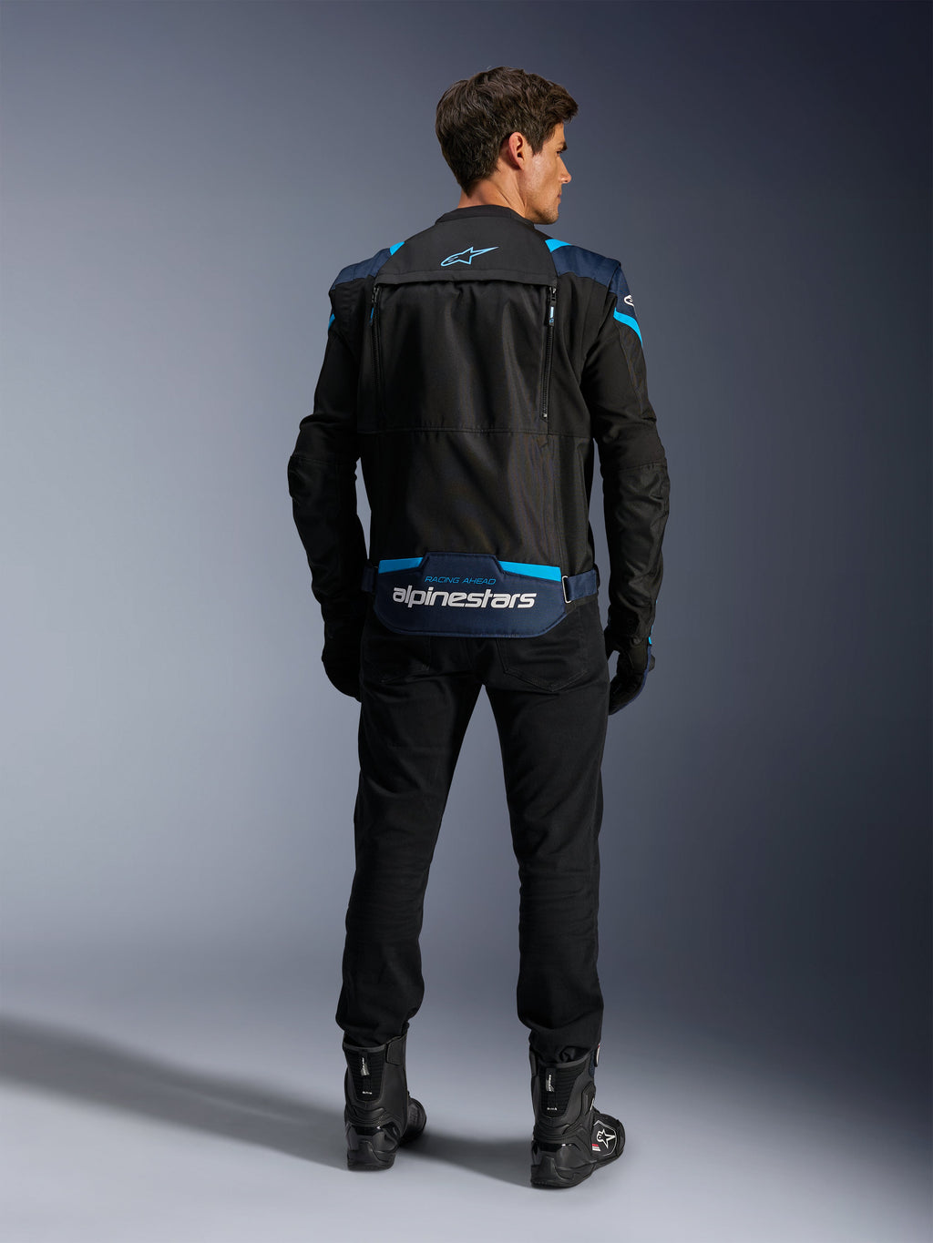 Alpinestars T-Stunt Air Jacket, Modular Textile Motorcycle Jacket, Black Dark Blue and Bright Blue, back view showing the lower back sleeve storage compartment with white Alpinestars branding, worn with black pants and boots.