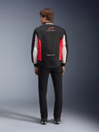 Alpinestars Monza Sport Jacket, Black Bright Red and White textile motorcycle jacket, rear view shown on a model, featuring red star logo and 'ASTARS' collar branding with slogans, worn with black pants and riding boots.