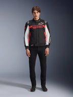 Male model wearing the Alpinestars Monza Sport Jacket in Black, Bright Red, and White, featuring a large red 'ASTARS' logo across the chest and white panels on the sleeves, paired with black pants and black riding boots.
