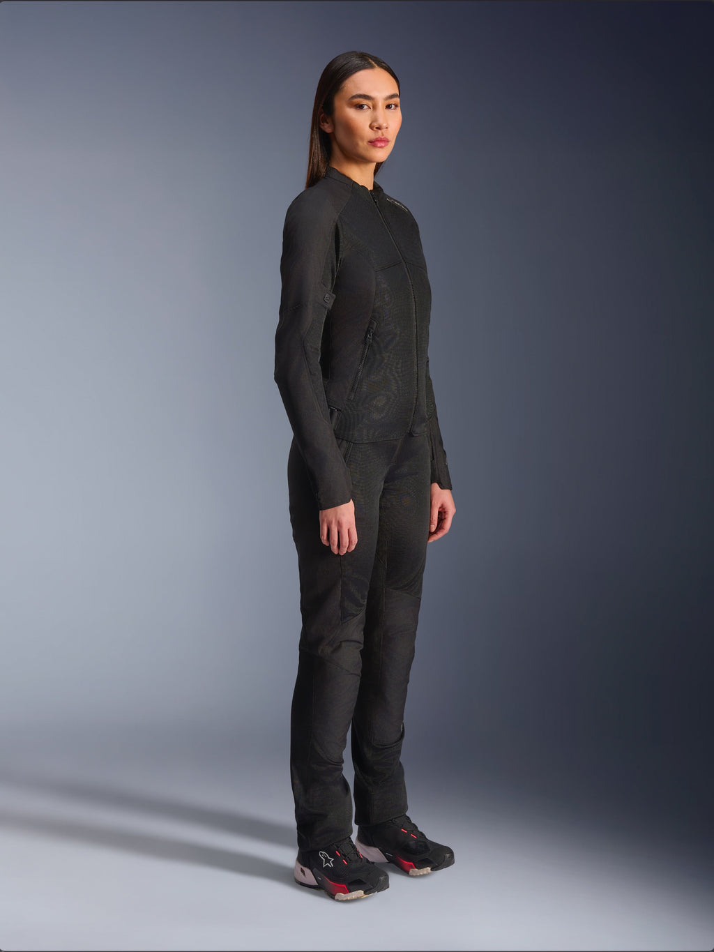 Alpinestars Woman Stella C-1 Air Jacket in Black, textile motorcycle jacket with mesh panels, worn with matching black riding pants and technical sneakers, studio shot showing a full-length urban riding outfit.