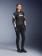 Female model wearing Alpinestars Stella T-GP Plus R V4 Jacket, Black and White, paired with black motorcycle pants, gloves, and boots, sleek sport-fit design for women riders