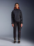 Alpinestars Actea Women's Pants, black motorcycle pants with red text detail and cargo pockets, worn by a female rider with a black hooded jacket, modern urban motorcycle apparel