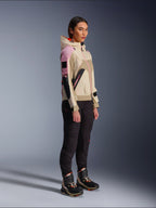 Female model wearing the Alpinestars Molly Air Jacket in Sand Pink Almond, paired with dark technical pants and high-top riding boots, urban motorcycle jacket featuring a hood and multi-color paneling, contemporary streetwear-inspired design