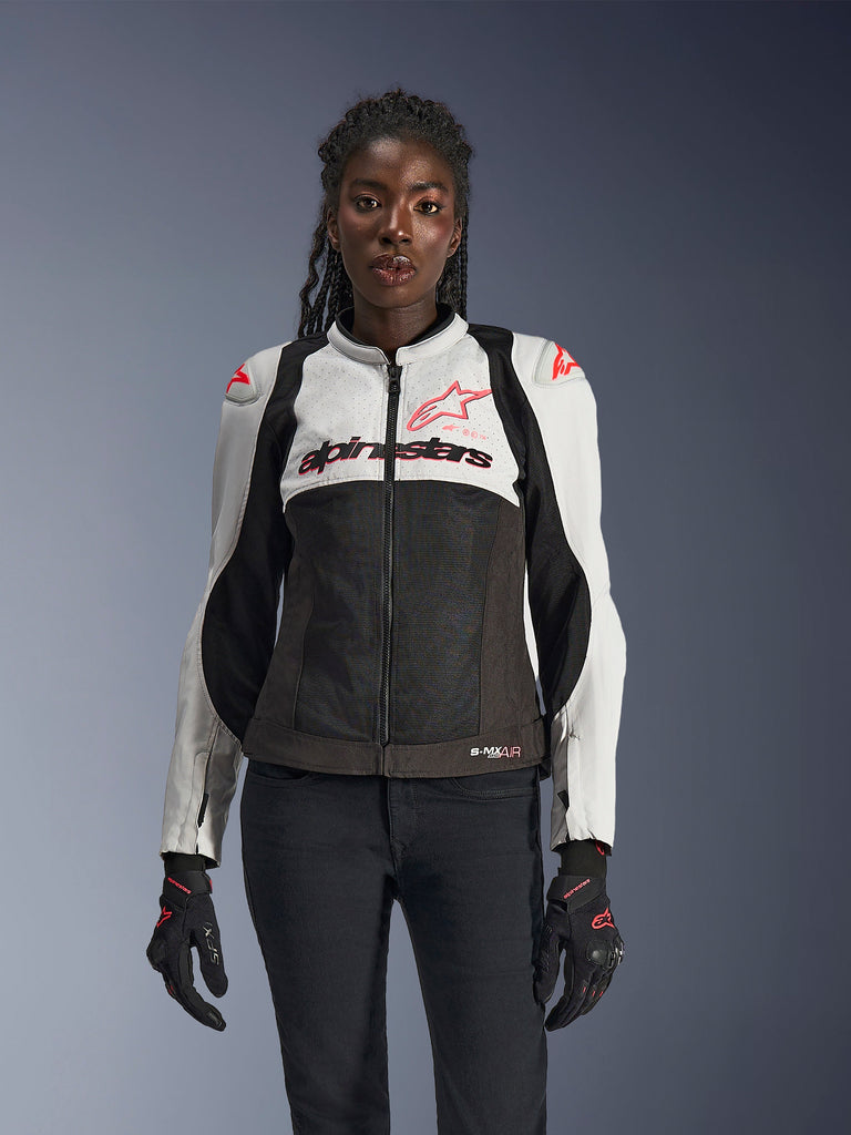 Alpinestars Woman Stella SMX Air Jacket, Ice Gray, Black, and Coral Fluo, featuring mesh construction and perforated panels, worn by a female model with black motorcycle gloves and pants, front view.