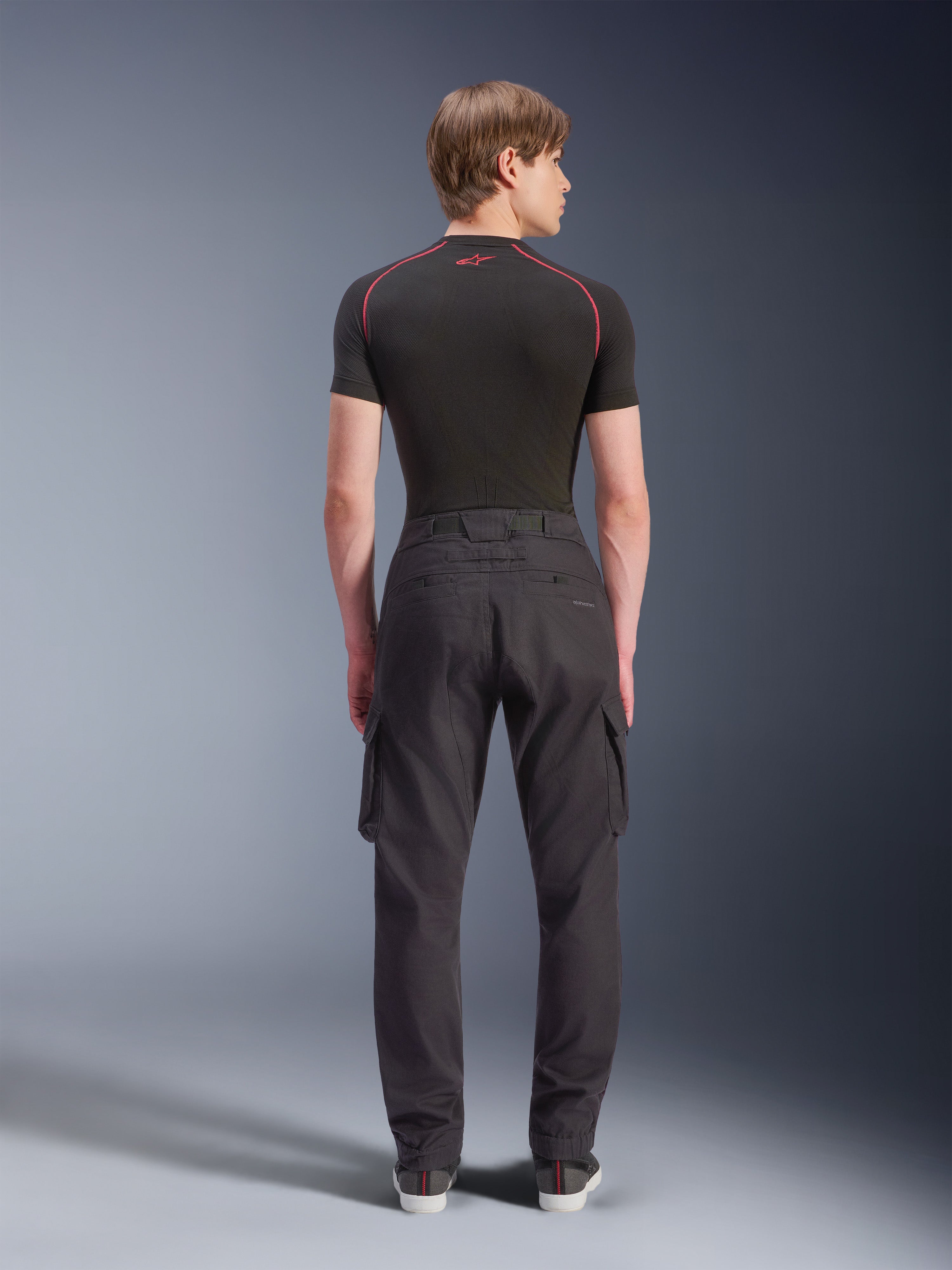 Alpinestars Flex-AST Cargo Pants, Motorcycle Cargo Pants, Black, rear view on model, featuring a regular tapered fit with elasticated hems and side cargo pockets, styled with a black base layer and casual sneakers