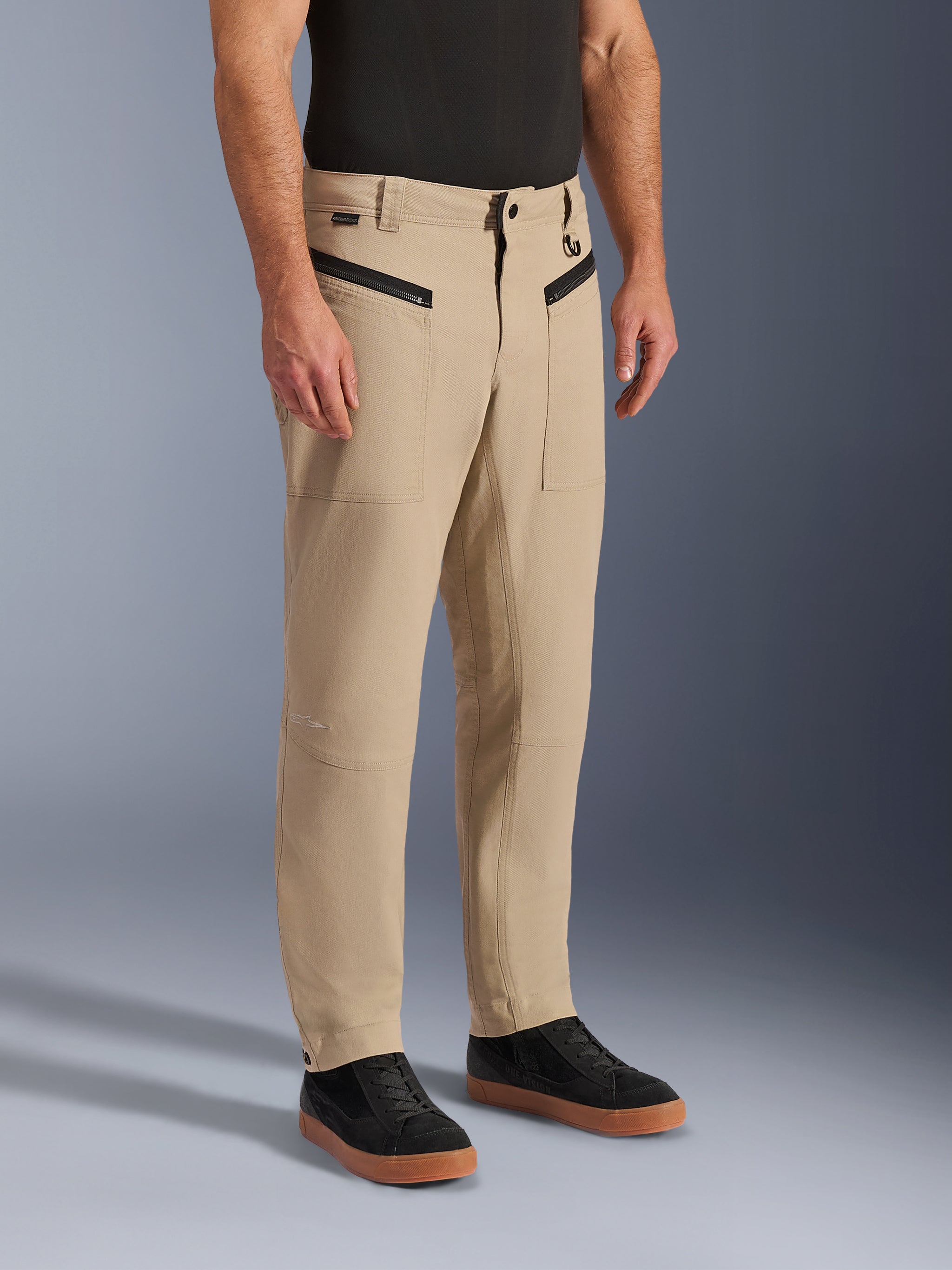 Alpinestars Flex-AST Canvas Pants, Urban Motorcycle Pants, Tan Brown, featuring heritage workwear styling with zippered front pockets and ergonomic knee panels, worn with black sneakers and a black t-shirt, contemporary urban riding gear