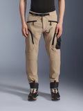 Alpinestars Acteon Pants, Urban Motorcycle Pants, Sand Beige, featuring a multi-pocket cargo design with black reverse coil zippers, integrated waist belt, and tapered fit, worn with black and orange boots.