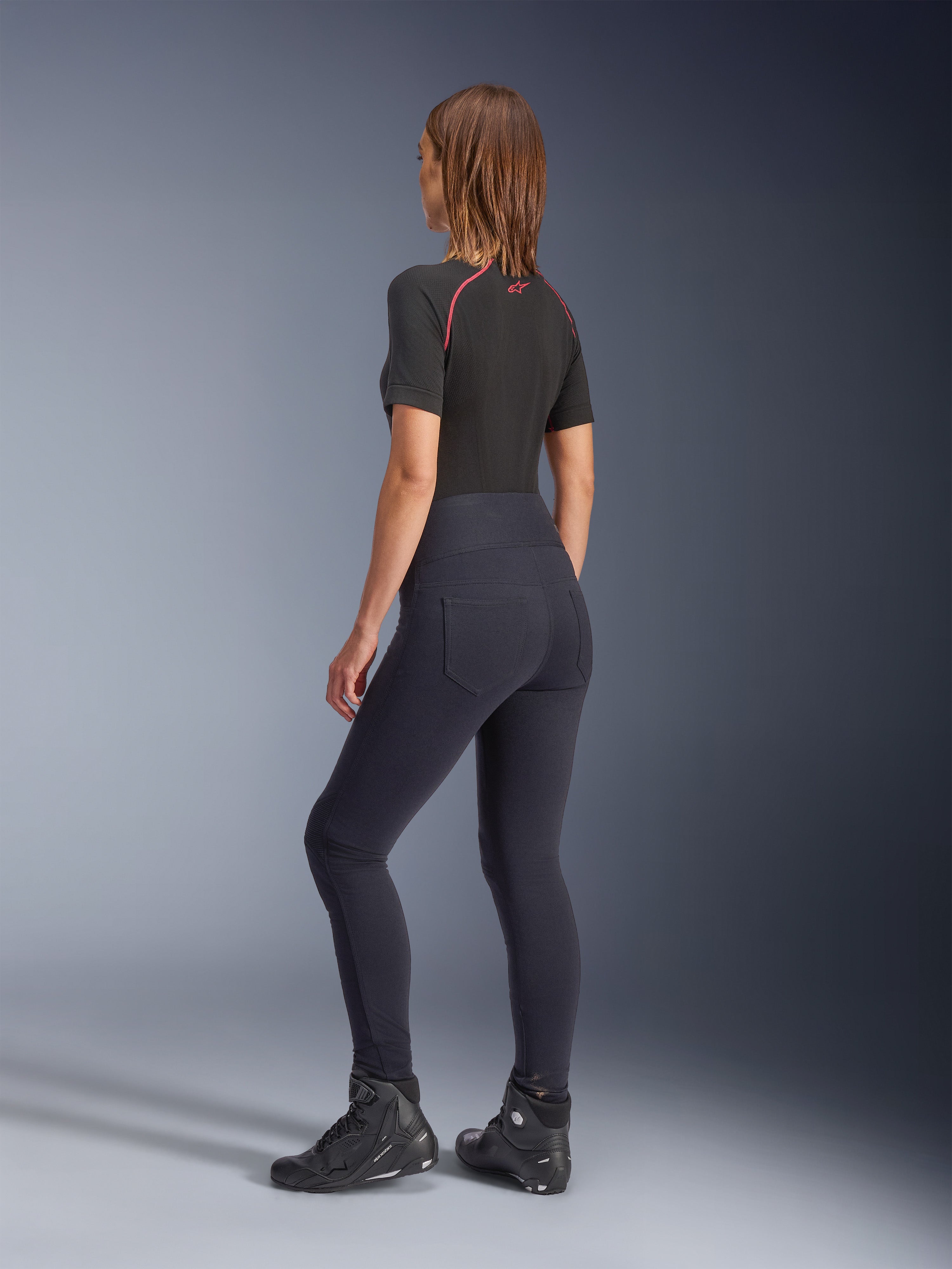 Alpinestars Woman Stella Flex-Ast Leggings, Black, rear view showing high-waisted fit and back pockets, worn with a black short-sleeve base layer with red accents and black motorcycle shoes, urban contemporary motorcycle gear