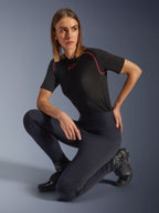 Alpinestars Stella Flex-Ast Leggings, Black, worn by a woman kneeling in a studio setting, paired with a black short-sleeve performance top with pink trim and black riding boots, featuring a high-waisted fit and flexible panels for urban riding.