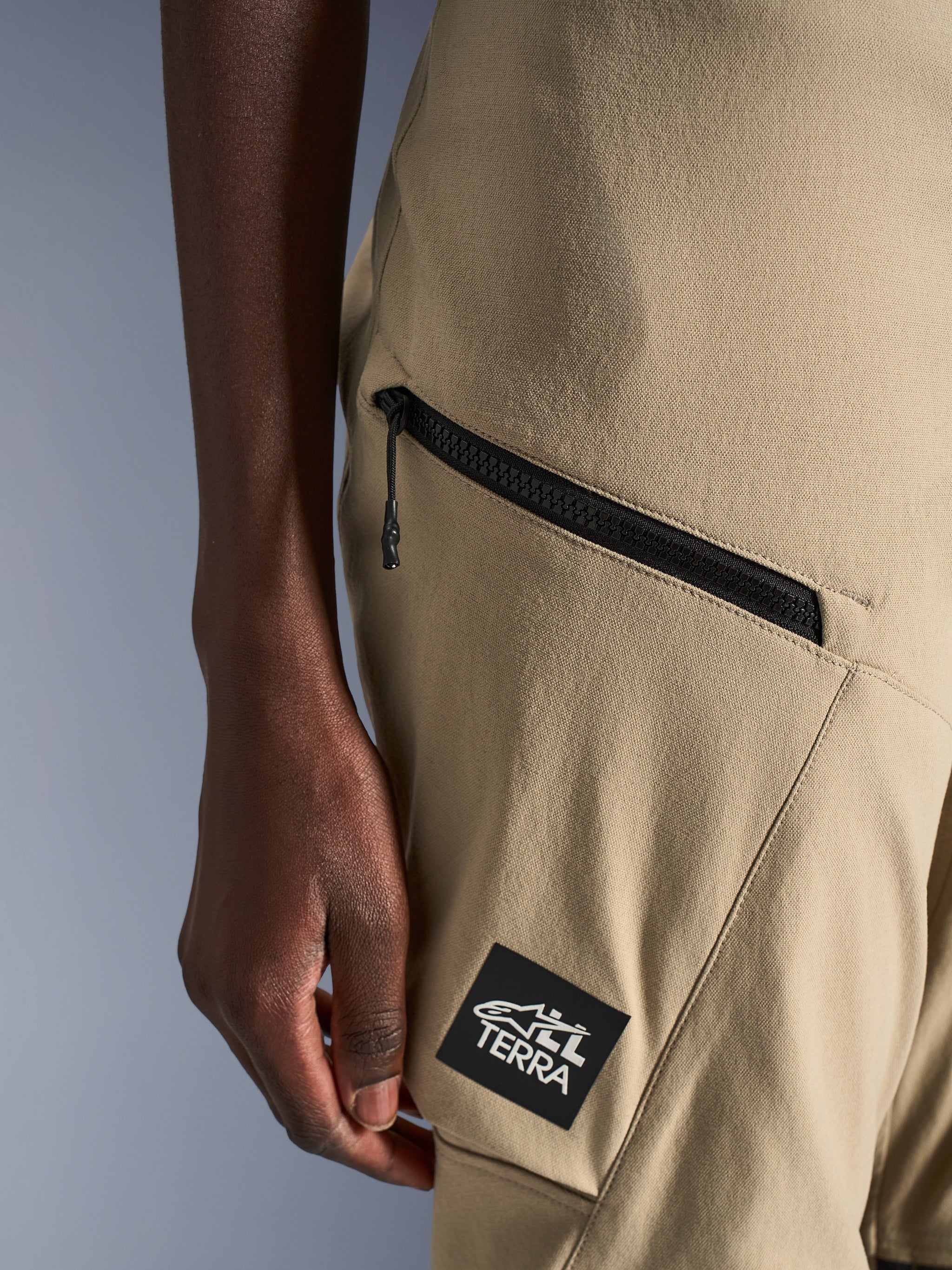 Alpinestars Stella Flex-AST Explorer Pants, Women's Motorcycle Pants, Sand, close-up detail of zippered cargo pocket and black ALL TERRA logo patch, durable ripstop textile construction for adventure touring