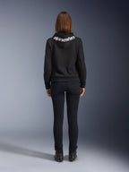 Daisy V3 Women's Riding Denim, Black Rinse, slim fit motorcycle pants, rear view showing high back waist and feminine silhouette, paired with a black Alpinestars hoodie and black riding boots, urban casual riding gear