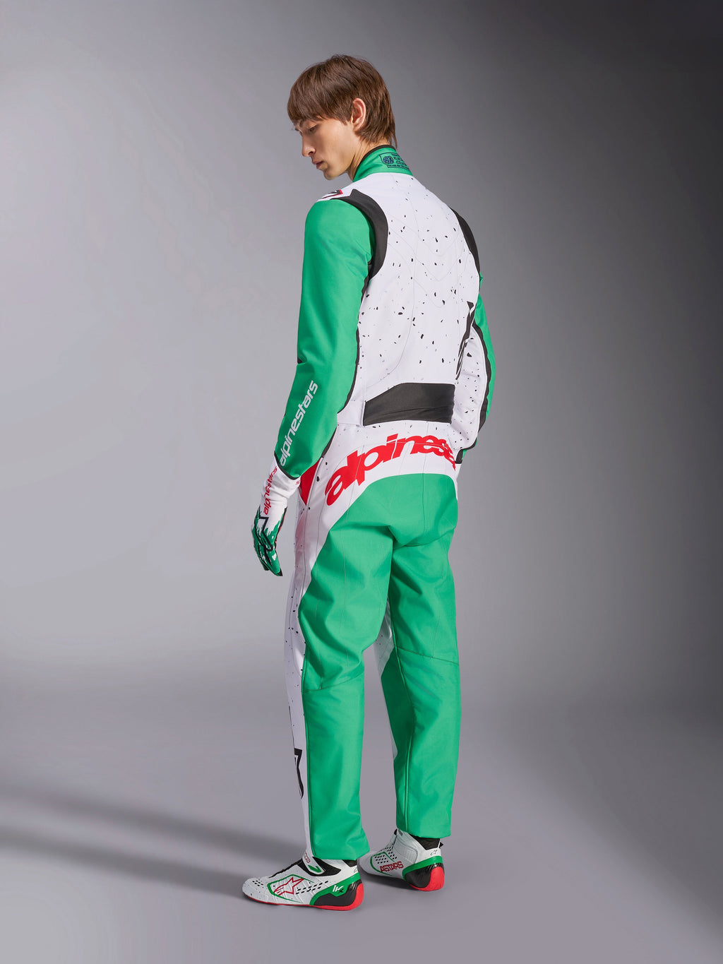 Alpinestars KMX-9 V3 Graphic 6 Suit, Karting Suit, White Green and Red, model viewed from the back-side, featuring green sleeves and lower panels, white upper torso with black speckle detail, bold red Alpinestars branding across the lower back, paired with matching white and green karting shoes.