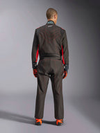Rear view of a driver wearing the Alpinestars KMX-9 V3 Suit, Karting Suit, Black with Red Fluo accents and red contrast stitching, professional motorsport racing gear, worn with orange and black racing gloves and shoes.