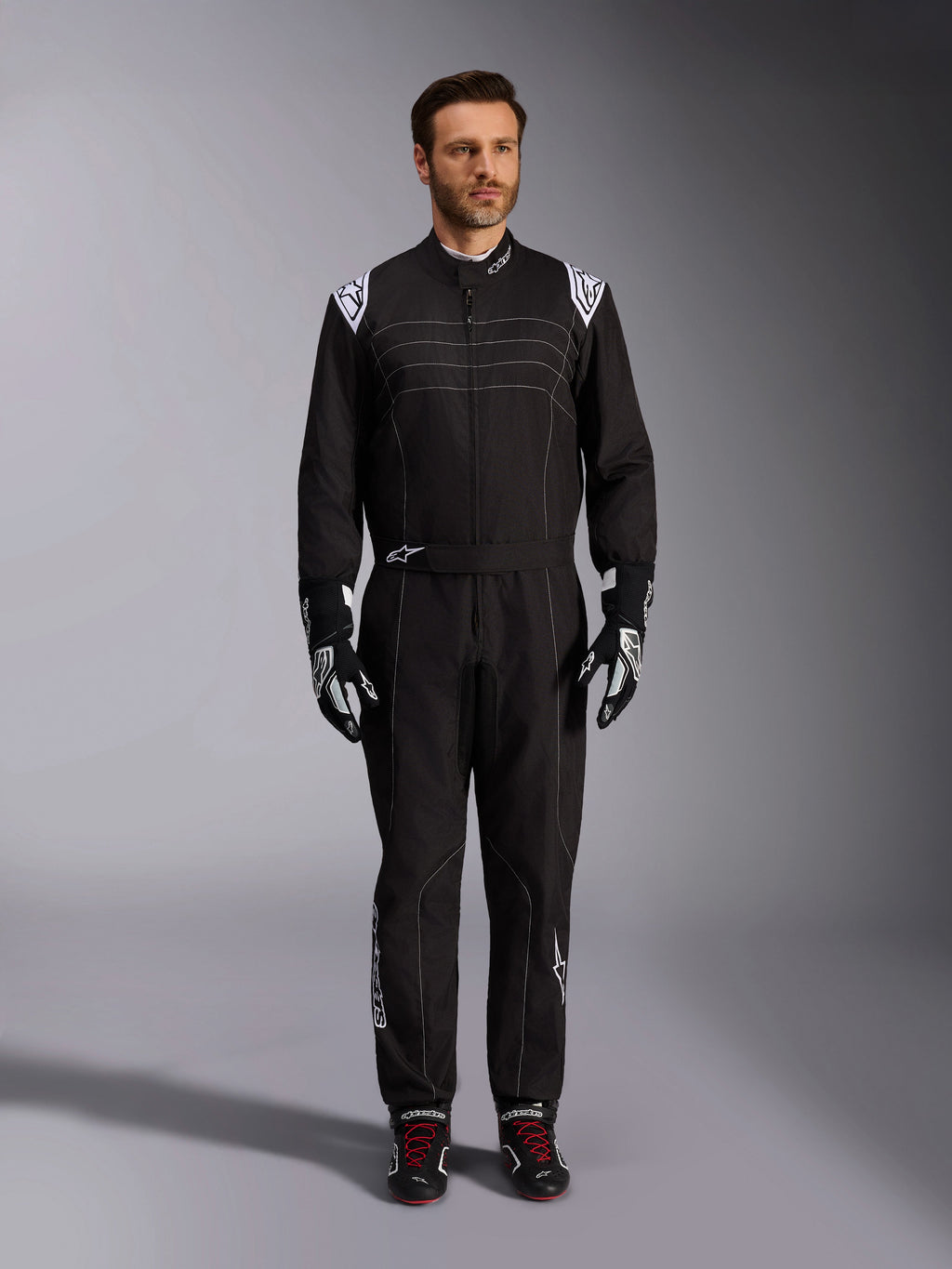Alpinestars KMX-9 V3 Suit, Black and White Karting Suit, full-length view on a model, featuring white shoulder logos and accents, styled with black and white racing gloves and black shoes with red laces, athletic-regular fit for professional karting gear.