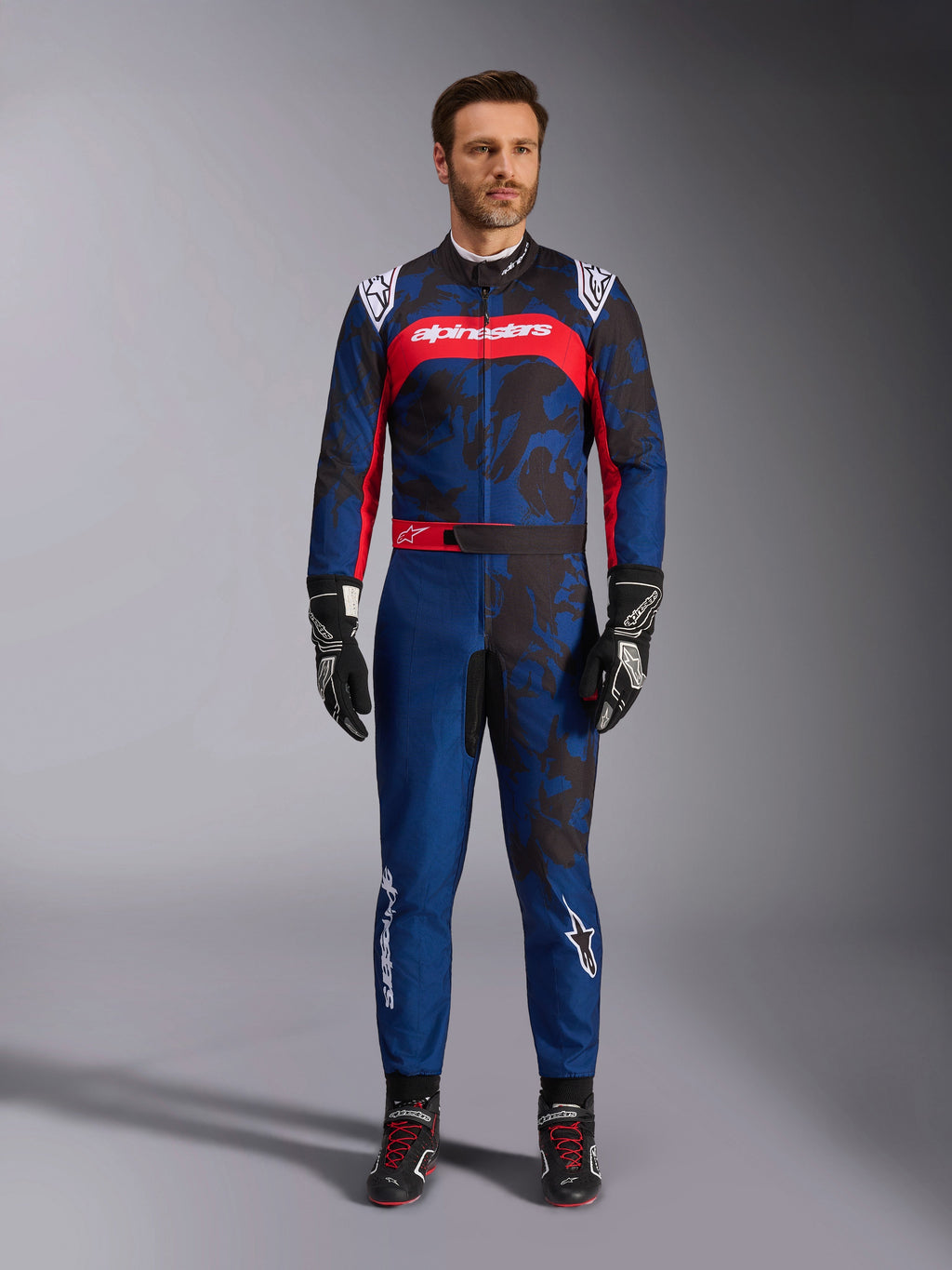 Alpinestars KMX-9 V3 Graphic 5 Suit, Karting Suit in Navy and Red, featuring an abstract camo-style graphic pattern, worn by a model with black racing gloves and shoes, athletic design with prominent Alpinestars branding on the chest and legs.