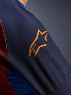 Alpinestars Maxdura Dual Jersey, close-up of the Mood Indigo sleeve with a yellow Alpinestars logo, showing integrated spacer mesh padding and Rust Brown mesh torso fabric, technical adventure motorcycle apparel