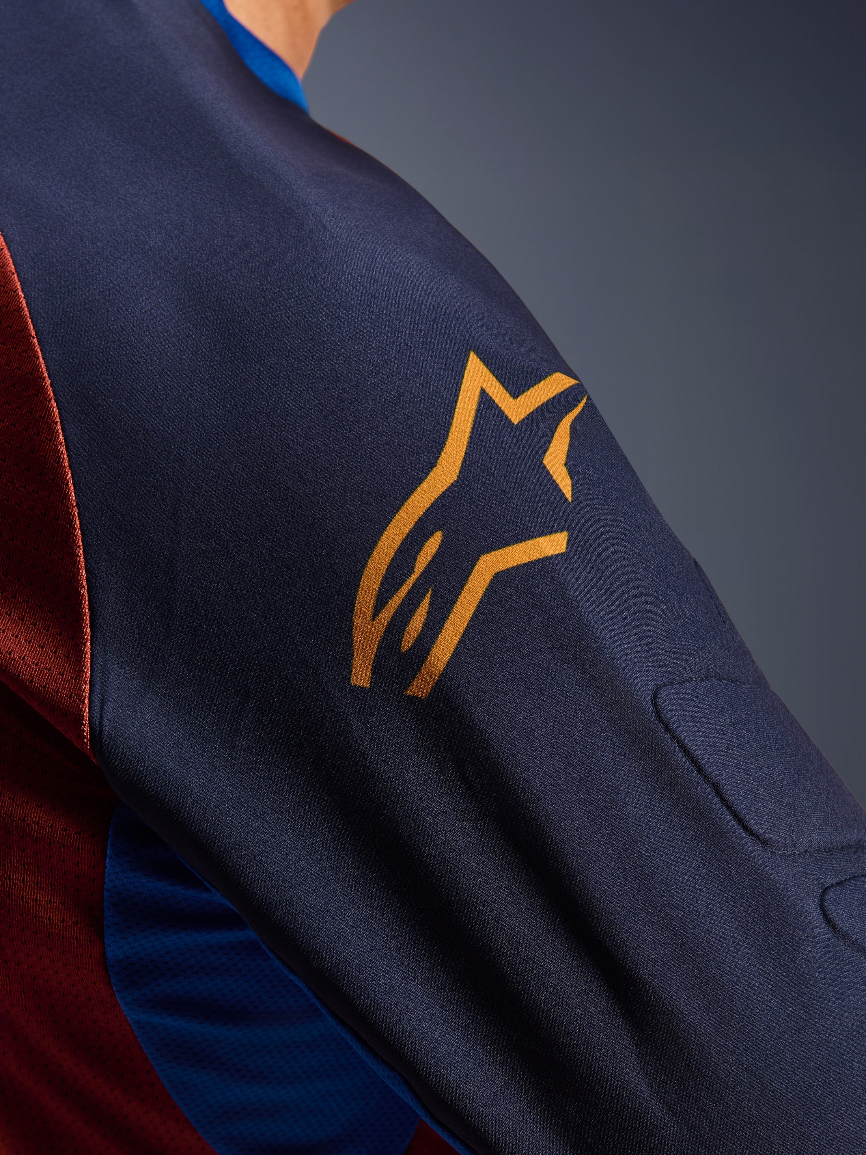 Alpinestars Maxdura Dual Jersey, close-up of the Mood Indigo sleeve with a yellow Alpinestars logo, showing integrated spacer mesh padding and Rust Brown mesh torso fabric, technical adventure motorcycle apparel