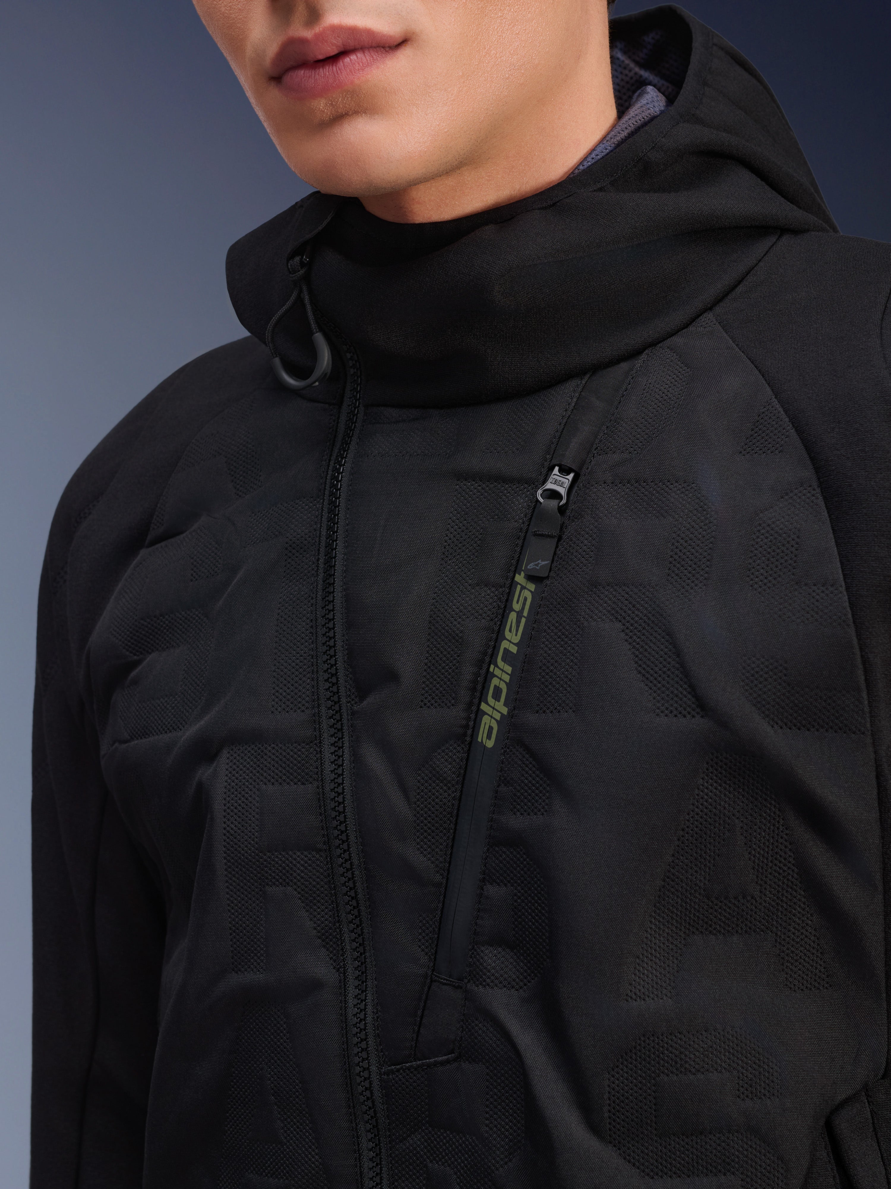 Alpinestars MO.ST.EQ Hybrid Hooded Jacket, Black, close-up view of angled front zipper with lime green branding, seamless padded chest panels, urban motorcycle streetwear