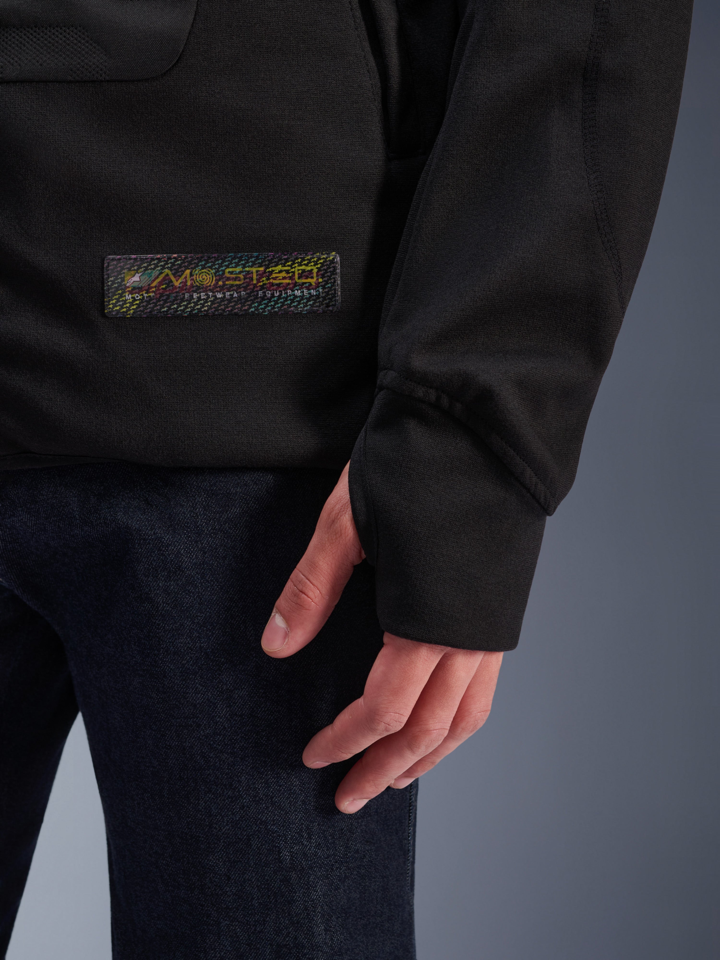 Alpinestars MO.ST.EQ Hybrid Hooded Jacket, Black, close-up of sleeve cuff with thumb loop, holographic MO.ST.EQ logo patch, urban streetwear motorcycle jacket