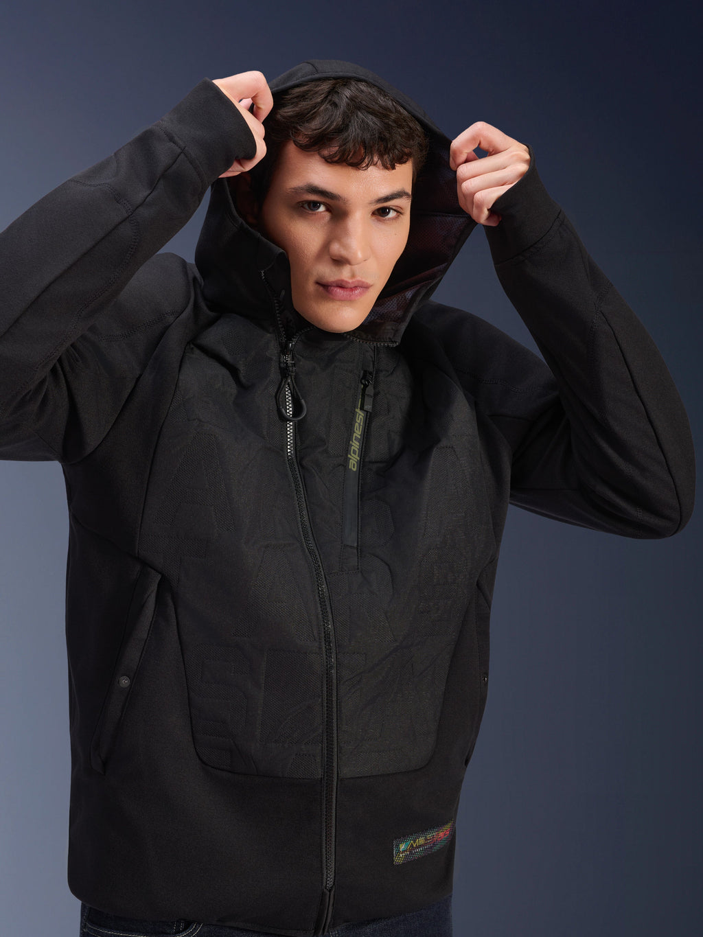 Alpinestars MO.ST.EQ Hybrid Hooded Jacket, Urban Motorcycle Jacket, Black, featuring padded panels and an angled front zipper, worn by a model with the hood up, modern streetwear-inspired protective clothing for riders