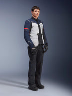 Alpinestars ST-7 2L GORE-TEX Jacket in Ice Gray, Dark Blue, and Black colorway with red accents, worn by a male model with black motorcycle pants and gloves, professional adventure touring motorcycle gear